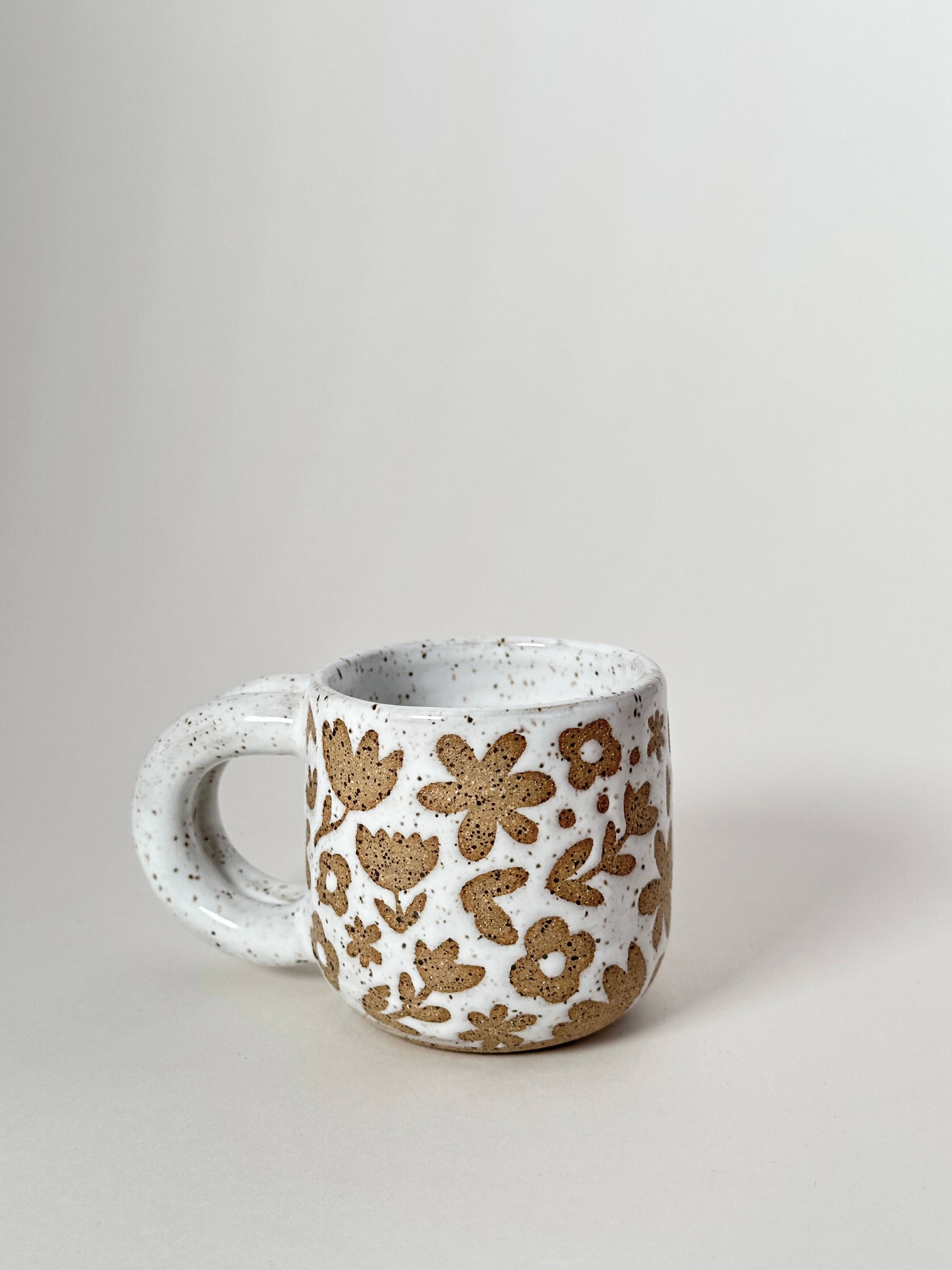 A small, speckled white and brown ceramic mug with a floral pattern.