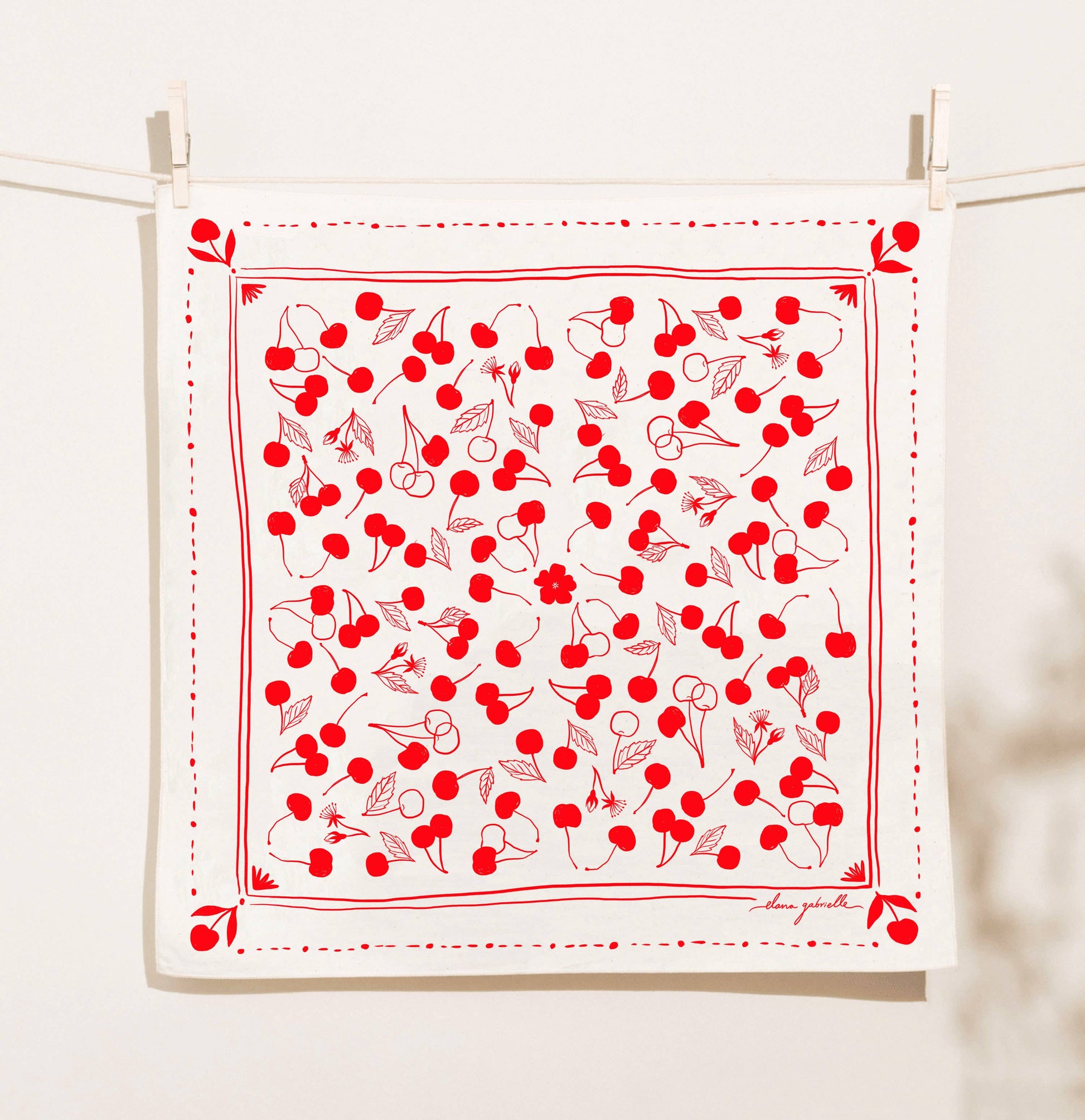 White fabric with red cherry pattern hanging on a line against a white background