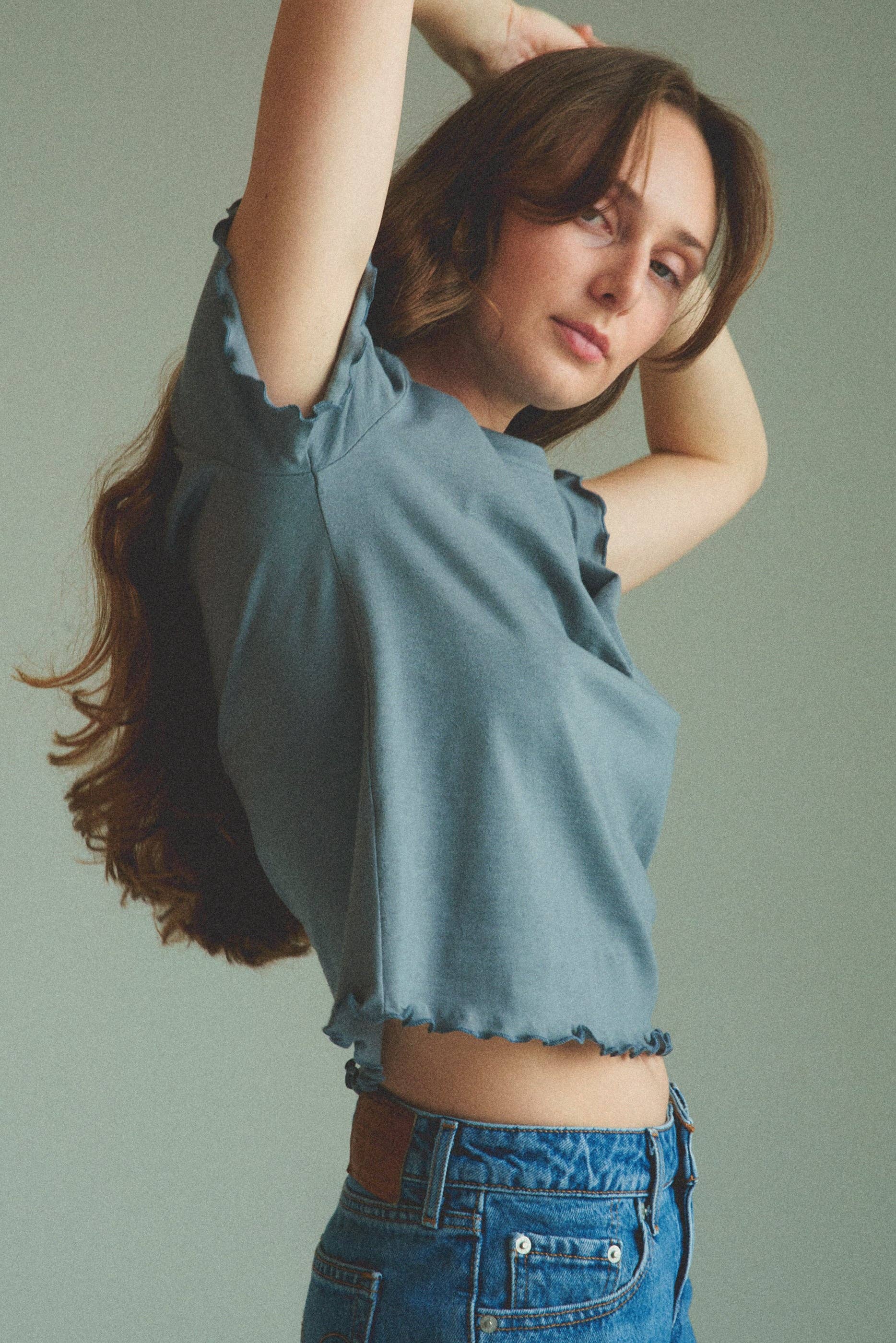 Woman wearing a blue top and jeans against a plain background