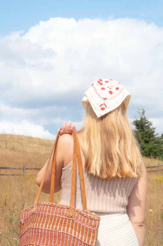 Person with a large bag and a hat with hearts in a field